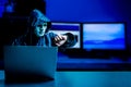 Anonymous computer hacker in white mask and hoodie. Obscured dark face using laptop computer for cyber attack and checking time , Royalty Free Stock Photo