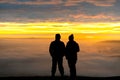 Anonymous couple standing on mountain together in love watching sunrise silhouetted stood high above clouds looking down valley Royalty Free Stock Photo