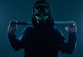 Anonymous criminal man with baseball bat in a black hoodie and neon mask