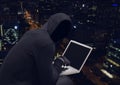 Anonymous Criminal Man in hood on laptop in front of night city