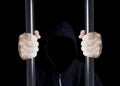 Anonymous criminal prisoner in hood holding prison bars