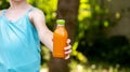 Anonymous elementary school age girl holding a glass bottle full of healthy natural orange juice, face obscured, copy space,