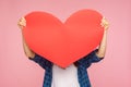 Anonymous girl hiding behind large paper heart, holding big greeting card and congratulating on Valentine`s day