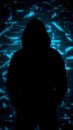 Anonymous hacker. Dark silhouette of a person in a hood against a background of blurred blue holographic pixels