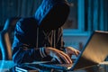 Anonymous hacker programmer uses a laptop to hack the system in the dark. Concept of cybercrime and hacking database