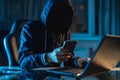 Anonymous hacker programmer uses a laptop to hack the system in the dark. Concept of cybercrime and hacking database