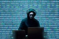 Anonymous hacker wearing face mask working on computer in dark room Royalty Free Stock Photo