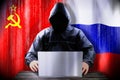 Anonymous hacker working on a laptop, flags of CCCP and Russian Federation