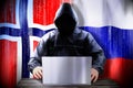 Anonymous hacker working on a laptop, flags of Norway and Russia Royalty Free Stock Photo