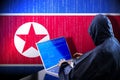 Anonymous hooded hacker, flag of North Korea, binary code - cyber attack concept
