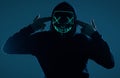 Anonymous man in black hoodie hiding his face behind a neon mask