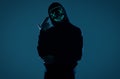 Anonymous man in black hoodie hiding his face behind a neon mask