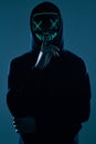 Anonymous man in black hoodie hiding his face behind a neon mask