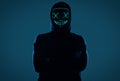 Anonymous man in black hoodie hiding his face behind a neon mask