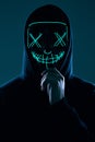 Anonymous man in black hoodie hiding his face behind a neon mask