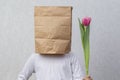 An anonymous man with a box on his head that limits his identity is holding a flower