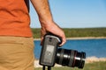 Anonymous man holding DSLR camera in hands next to seashore, no face, body detail