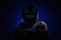 Anonymous man in hoodie hiding face behind neon glow scary mask on dark background. Horror concept Royalty Free Stock Photo