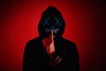 Anonymous man in hoodie hiding face behind neon glow scary mask on red background. Horror concept Royalty Free Stock Photo