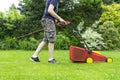 Anonymous man mowing green grass with lawn mower in backyard on a summer day. Seasonal garden work concept Royalty Free Stock Photo