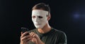 Anonymous masked fraudster demands a ransom for blackmail using a smartphone. Masked Criminal intimidates the victim