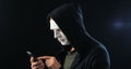 Anonymous masked fraudster in hood demands a ransom for blackmail using a smartphone. Masked Criminal intimidates the