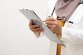 Anonymous muslim female doctor wearing hijab with stethoscope in white coat holding clipboard, ready to serve her medical patient