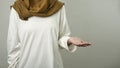 Anonymous muslim female showing empty palm hand on side of her body, against grey background with copy space, gesture of