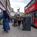 An Anonymous Muslim Woman Wearing A Traditional Hijab Walking Along A Town Centre High With People