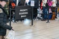 Anonymous passengers in queue behind PRIORITY BOARDING sign at the airport. All brands logos removed