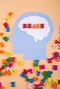 An anonymous person. Blue silhouette of a paper head with worfd Brain written by colorful wooden letters on light beige background