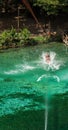 Person ziplining over clear green water, creating splashes.