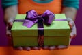 Anonymous person offering a gift wrapped in bright green with a purple ribbon