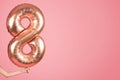 An anonymous person& x27;s hand holding a large, shiny rose gold number eight balloon