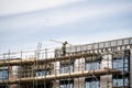 Scaffolder in PPE erecting framework of wooden planks and tall scaffolding poles high up on modern new building construction site Royalty Free Stock Photo