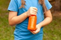 Anonymous school age girl, child holding a glass bottle full of orange juice, simple vegetable juice, hands closeup. Healthy