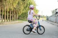 Anonymous school age girl riding an old used retro second hand repurposed bike on an empty country road, summer vacations, rural