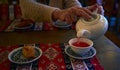 Anonymous woman pours tea from a white ceramic teapot into a cup and paklava in a plate on a restaurant table. Restaurant with Royalty Free Stock Photo