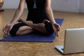 Woman sitting in padmasana on yoga mat in front of laptop in studio Royalty Free Stock Photo