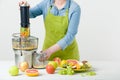 Anonymous woman wearing an apron, preparing healthy fruit juice using modern electric juicer, healthy lifestyle concept