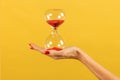 Unrecognizable woman holding hourglass in hand against yellow backdrop Royalty Free Stock Photo