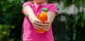 Anonymous young unrecognizable school age child, girl holding a glass bottle full of orange vegetable juice in hands, wide shot