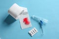 Anoscope, suppositories and toilet paper with red feather on blue background, flat lay. Hemorrhoid treatment