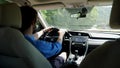 Man cabbie in a blue shirt and glasses drives a car on a hot summer day