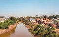 Antananarivo, Madagascar - May 07, 2019: Sun shines on simple houses near small muddy river, few Malagasy people walking by,