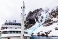 Antarctic cruise ship front view with mast and huge steep stone rock covered with glacier, close to Argentine islands, Antarctica Royalty Free Stock Photo