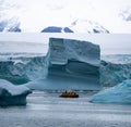 Antarctic expedition, cruise passengers in yellow parkas ride in a Zodiac inflatable boat, very close to a huge white Royalty Free Stock Photo