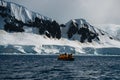 Antarctic expedition, cruise passengers in yellow parkas ride in a Zodiac inflatable boat, very close to a huge white Royalty Free Stock Photo