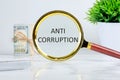 ANTI CORRUPTION text writing through a magnifying glass on a light background near a roll of money and a pot of green grass Royalty Free Stock Photo