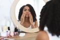 Anti-Wrinkle Skincare. Upset Black Woman Touching Her Face, Looking In Mirror Royalty Free Stock Photo